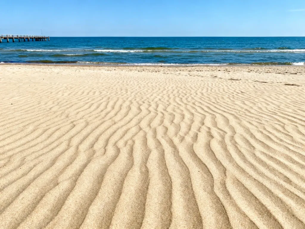 Słoneczna plaża w Chłopach z widokiem na spokojne morze i drewniane molo w letni dzień.